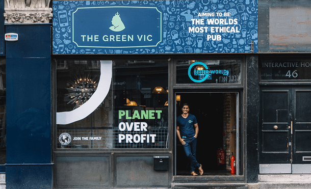 A man standing proudly in the doorway of The Green Vic pub displaying a planet over profit window sign representing the launch of our pioneer ethical hospitality concept in