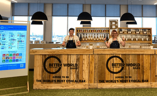 Three professional team members smiling and giving a thumbs up behind a large rustic wooden event bar representing our industry leading ethical hospitality service