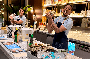 Two smiling bartenders shaking cocktails behind a sleek modern office coffee bar counter transformed for a corporate networking event