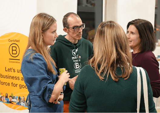 Four guests networking and discussing business as a force for good next to a B Corp certified pull up banner at the sustainable event