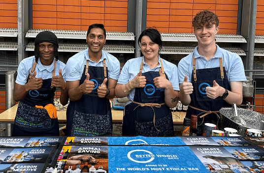 Four Better World staff in branded aprons giving a thumbs up behind the B Lab event bar
