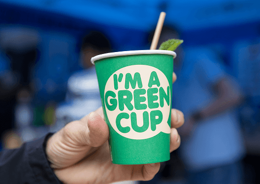 A close up of a hand holding a green eco disposable cup filled with a fresh cocktail
