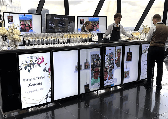 The digital wedding bar seen along its length, staff serving behind rows of filled champagne flutes on the polished floor