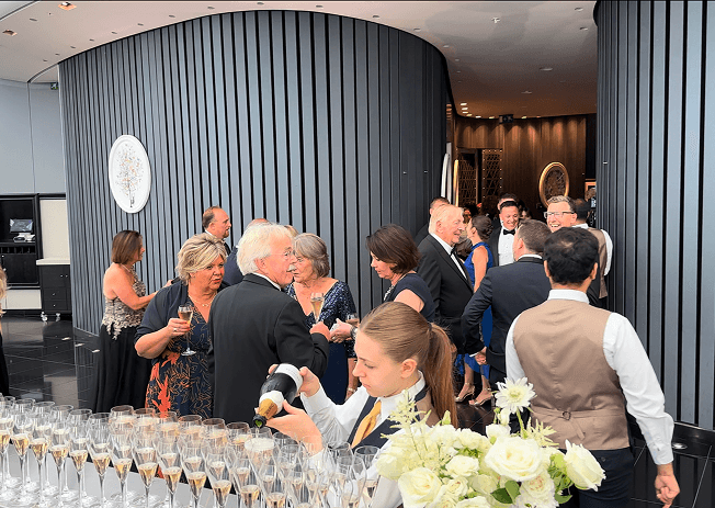Guests arriving and mingling in the curved panelled reception room as staff pour the champagne service in the foreground