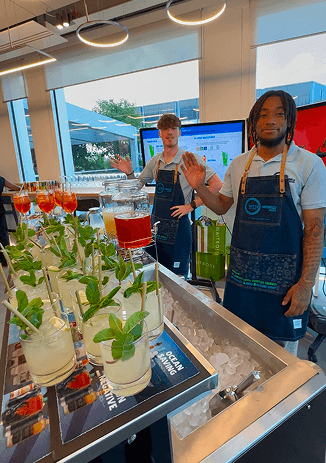 A Better World bartender in a branded apron waving beside a tray of freshly made mojitos on ice