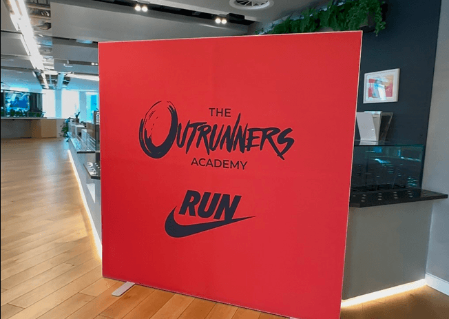 A large red event backdrop displaying the Outrunners Academy logo and the Nike