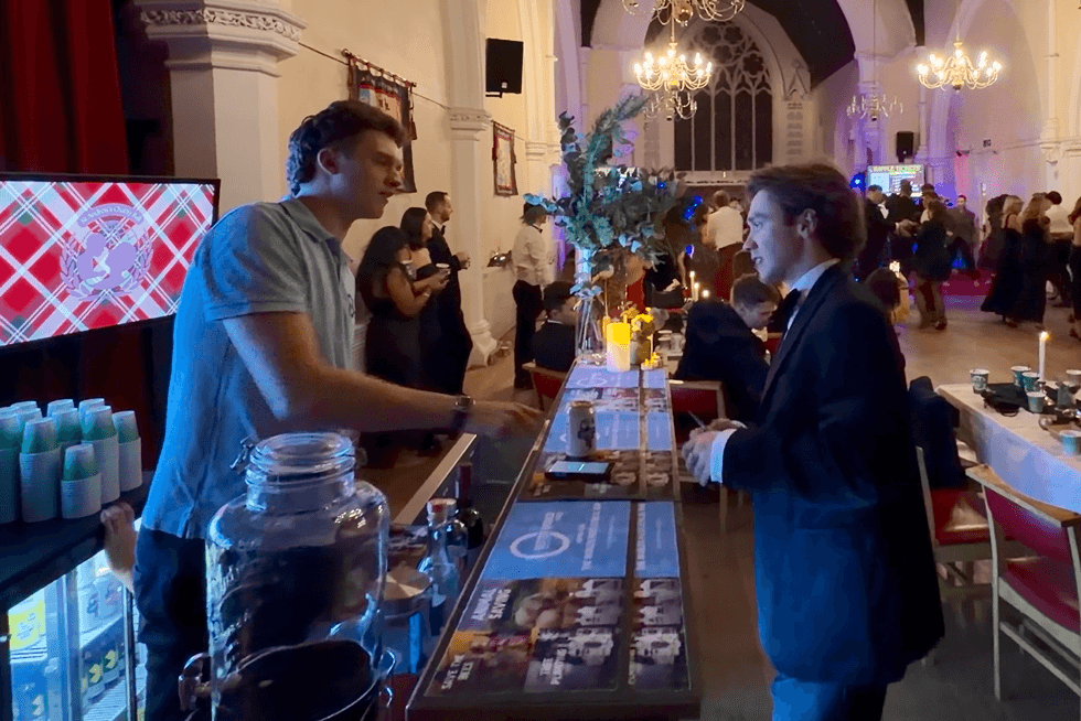 The event organiser talking with a bartender at the blue-lit charity ball bar