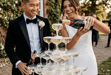 A happy newly married couple pouring a bottle of Moet champagne into the top of a large glowing champagne tower at their wedding reception to represent our picture perfect toast service
