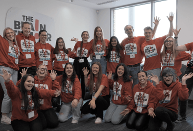 A large group of smiling charity workers wearing The Brain Tumour Charity clothing and cheering together representing the tangible social impact detailed in your personalised event report