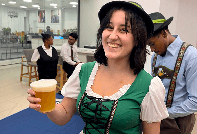 A smiling professional bartender in a traditional Oktoberfest outfit serving a fresh pint of beer while our expert team provides seamless hospitality service for a corporate office party