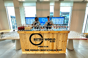 Two expert mixologists giving a thumbs up behind a rustic sustainable event bar covered in premium cocktails ready for an eco friendly celebration