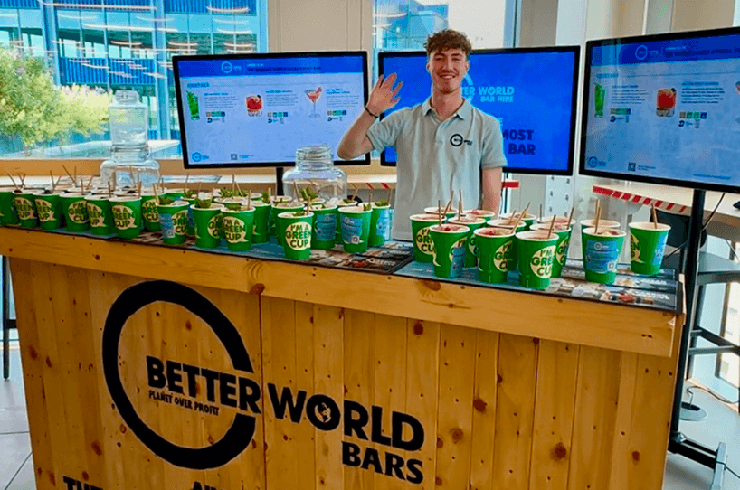 A professional bartender waving behind a rustic wooden event bar providing flawless sustainable hospitality for a corporate event in London